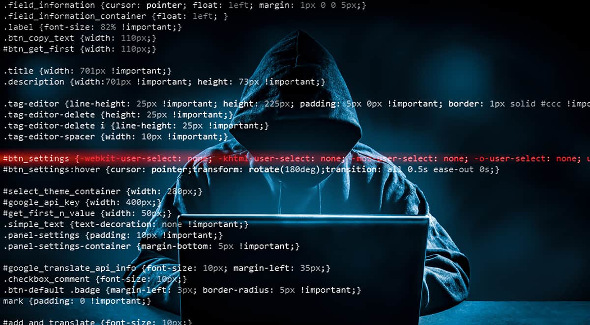 Person in a hood sitting in front of a computer in a dark room website hacking